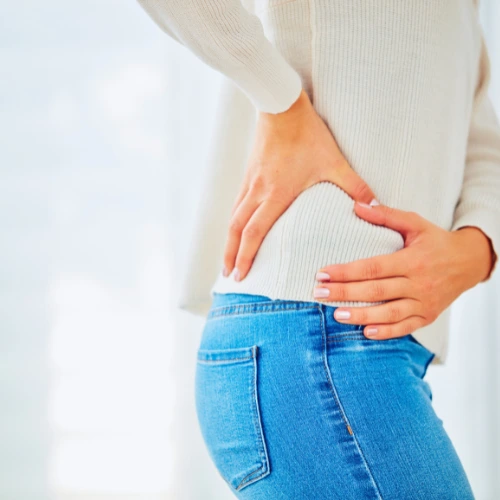 Woman in a white long-sleeved shirt and jeans holding her hip - back pain from weight loss chiropractic care in Hiram, GA.