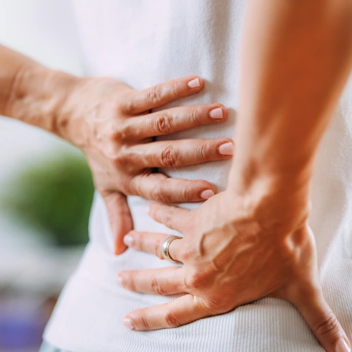 Woman in a white t-shirt holding her lower back - back pain from weight loss chiropractor in Hiram, GA.